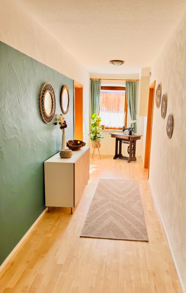 Heller Flur mit grüner Wand, Sideboard, Tisch und Pflanzen.